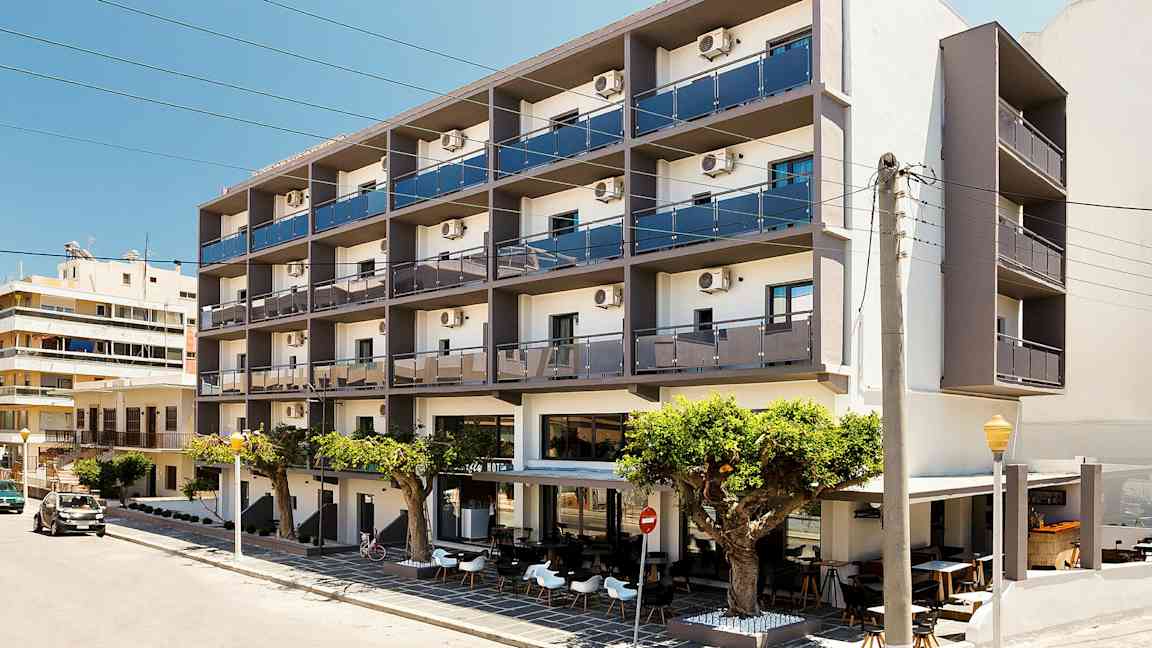 Et fleretasjes hotell med balkonger og uteservering foran, plassert ved en gate. (AI-generert tekst)