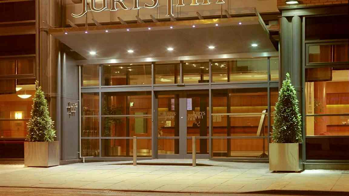 Hotellinngang med glassdører og skiltet 'Jurys Inn' over. (AI-generert tekst)