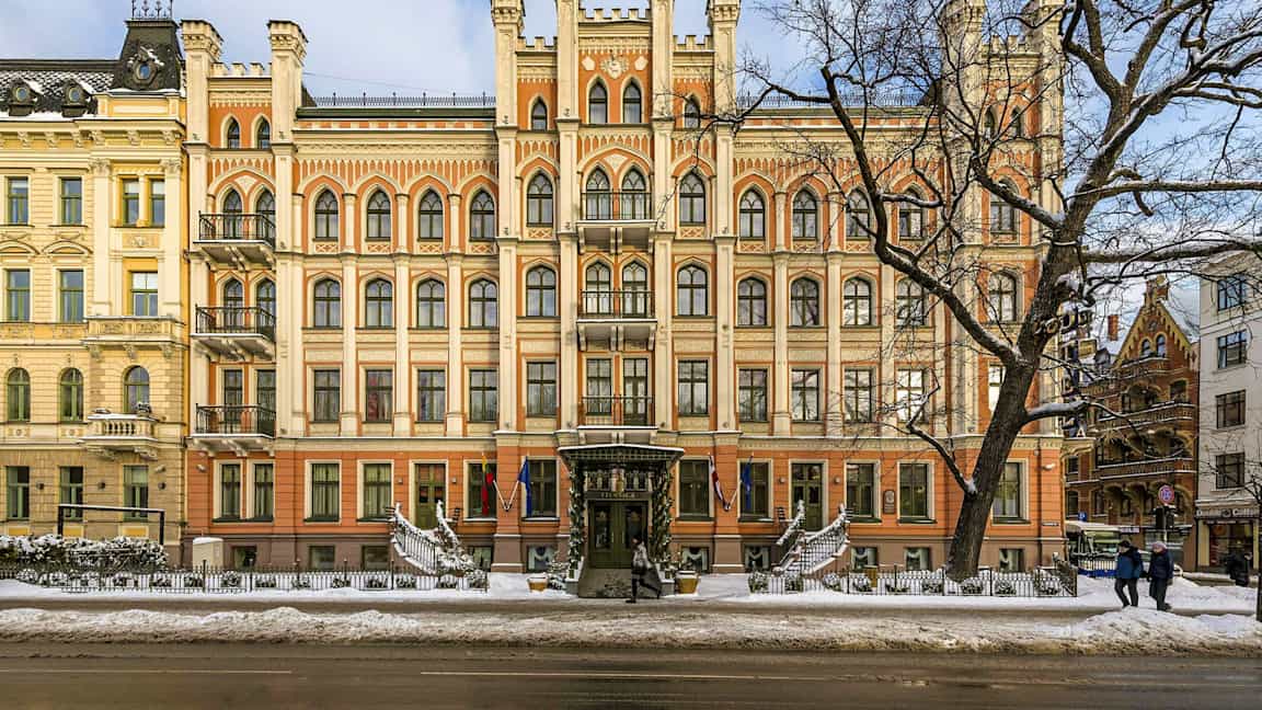 Fasaden til en staselig bygning med gotisk arkitektur og mange vinduer, sett på vinterstid med snø på bakken. (AI-generert tekst)
