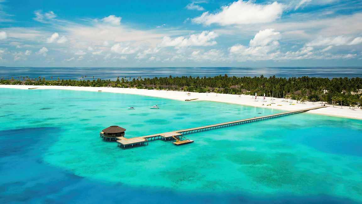 Flyfoto av en tropisk strand med en brygge som strekker seg over turkis vann. (AI-generert tekst)
