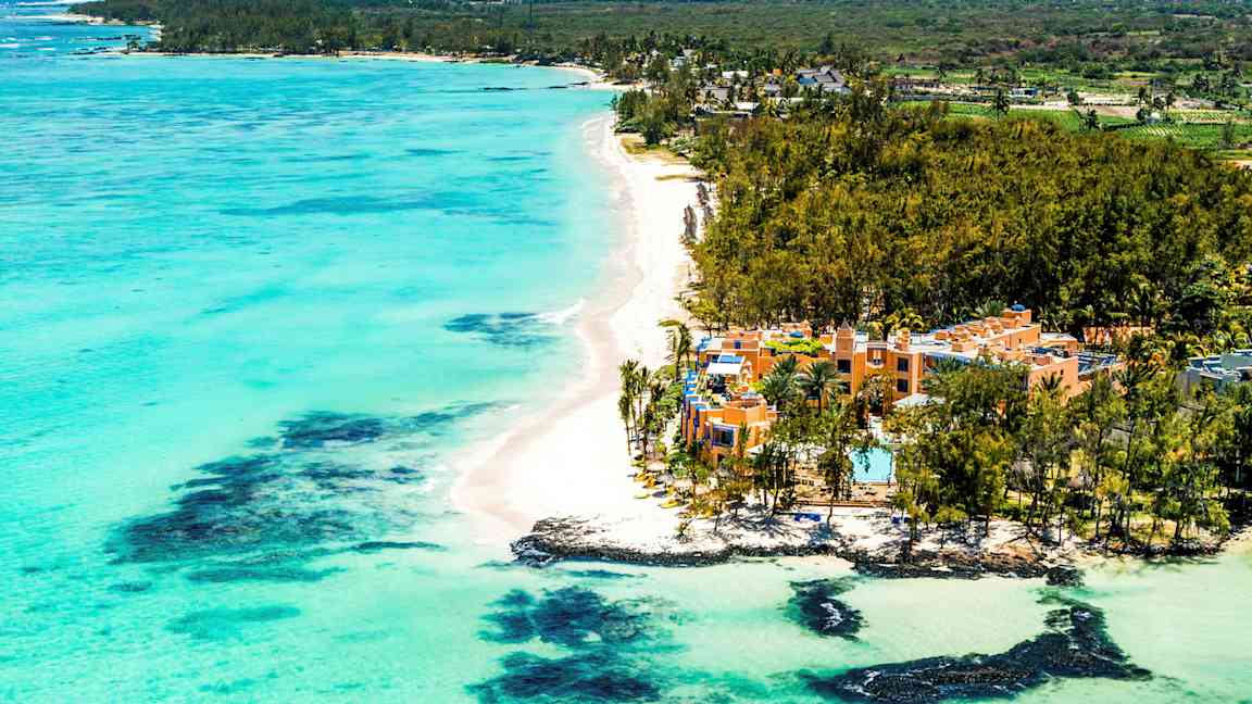 En sandstrand med turkist vann og hotell omgitt av grøntområde. (AI-generert tekst)