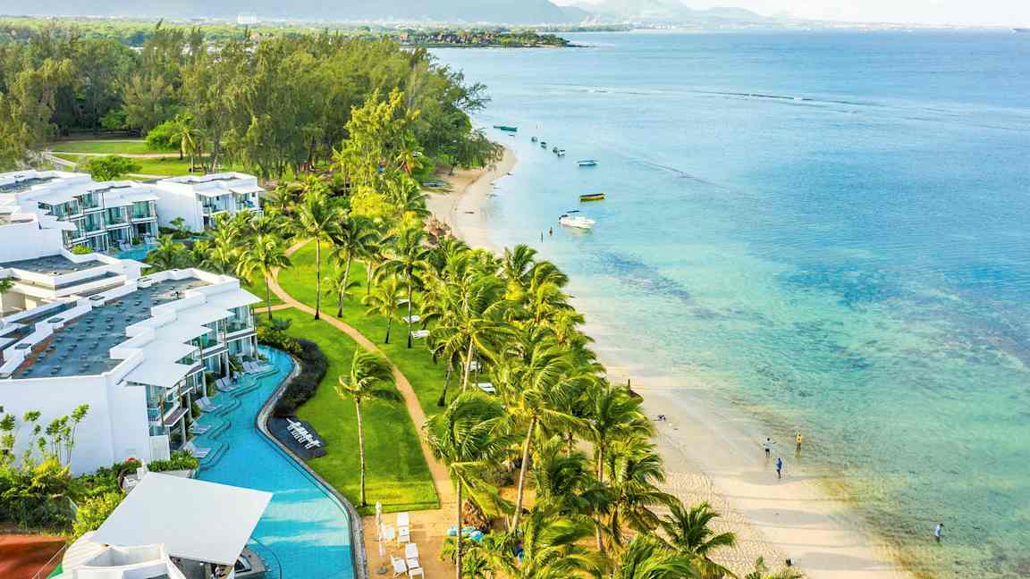 Et kystlandskap med hvite bygninger, palmer, sandstrand og turkist hav. (AI-generert tekst)