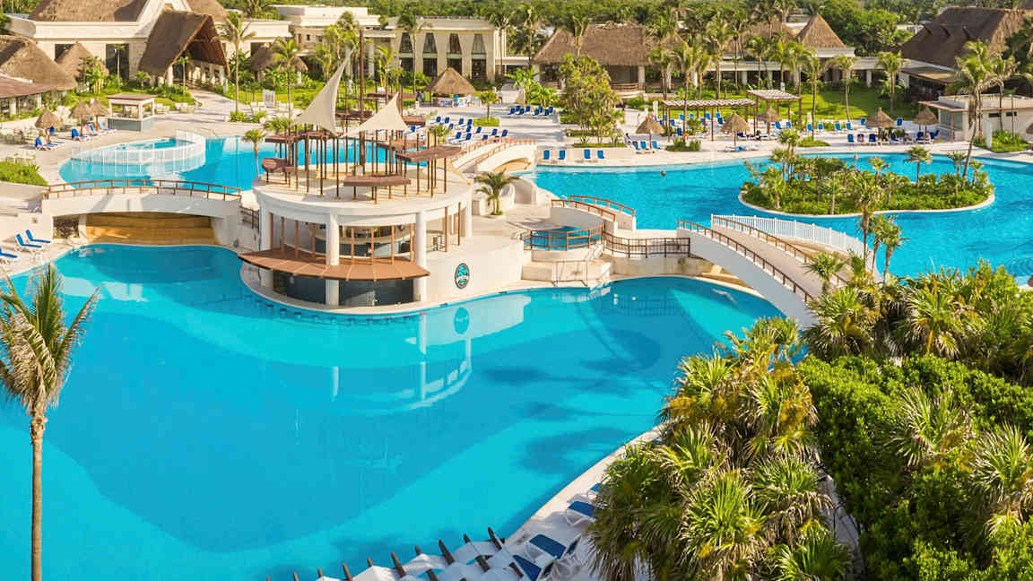 Et stort basseng med broer og et sentralt område omgitt av tropiske planter og bygninger. (AI-generert tekst)