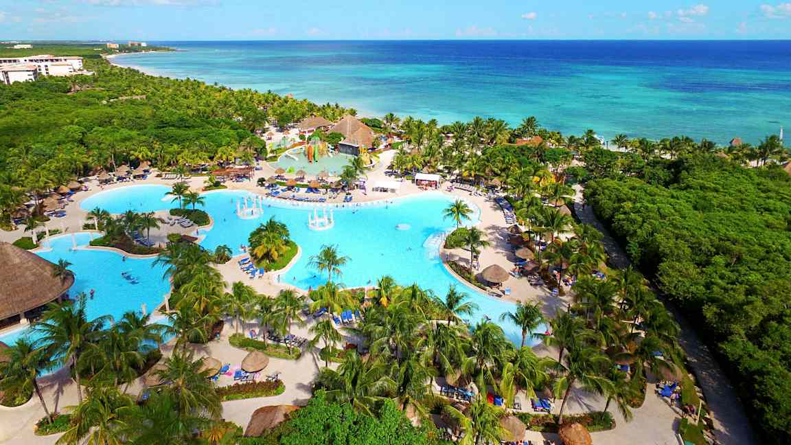 Luftfoto av et feriested med tropiske palmer, store svømmebassenger og nærhet til havet. (AI-generert tekst)