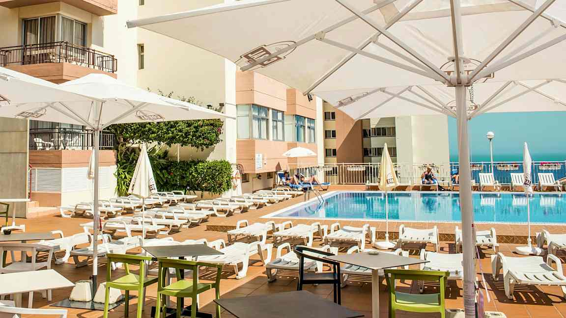 Utendørs bassengområde med solsenger og parasoller ved et hotell. (AI-generert tekst)