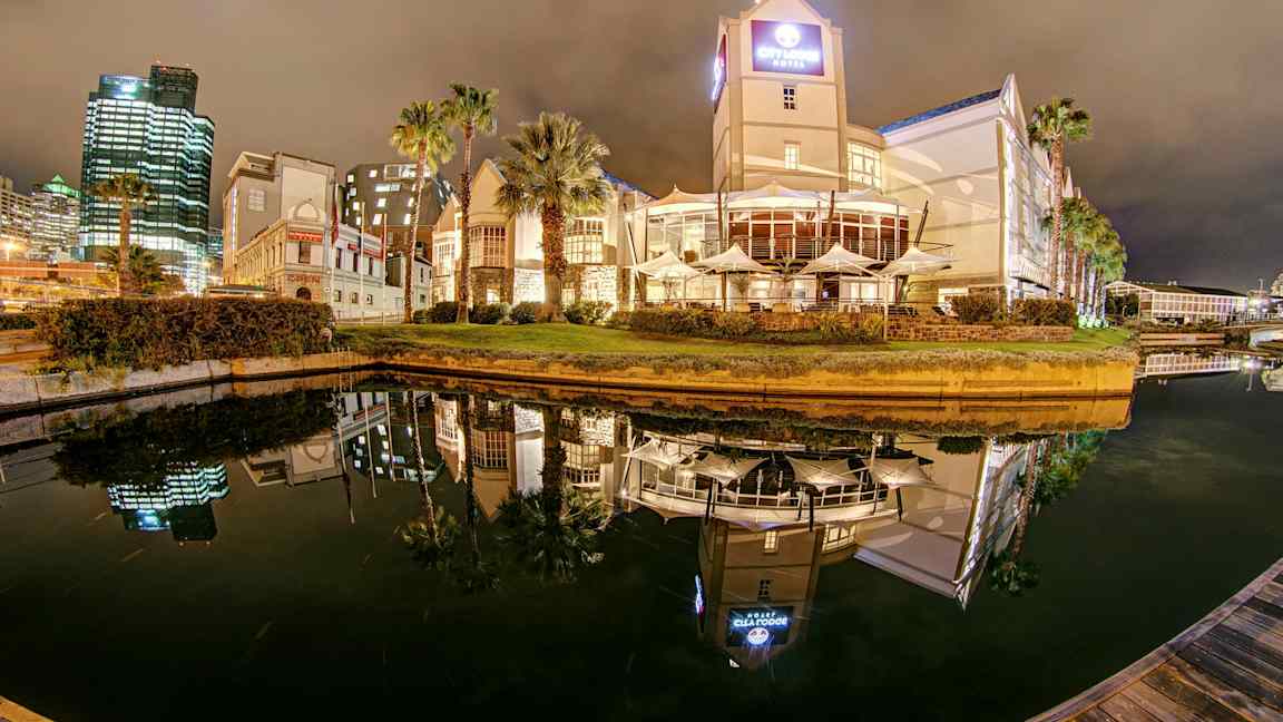 Hotell og bygninger ved en vannkanal om natten med speilrefleksjoner i vannet. (AI-generert tekst)