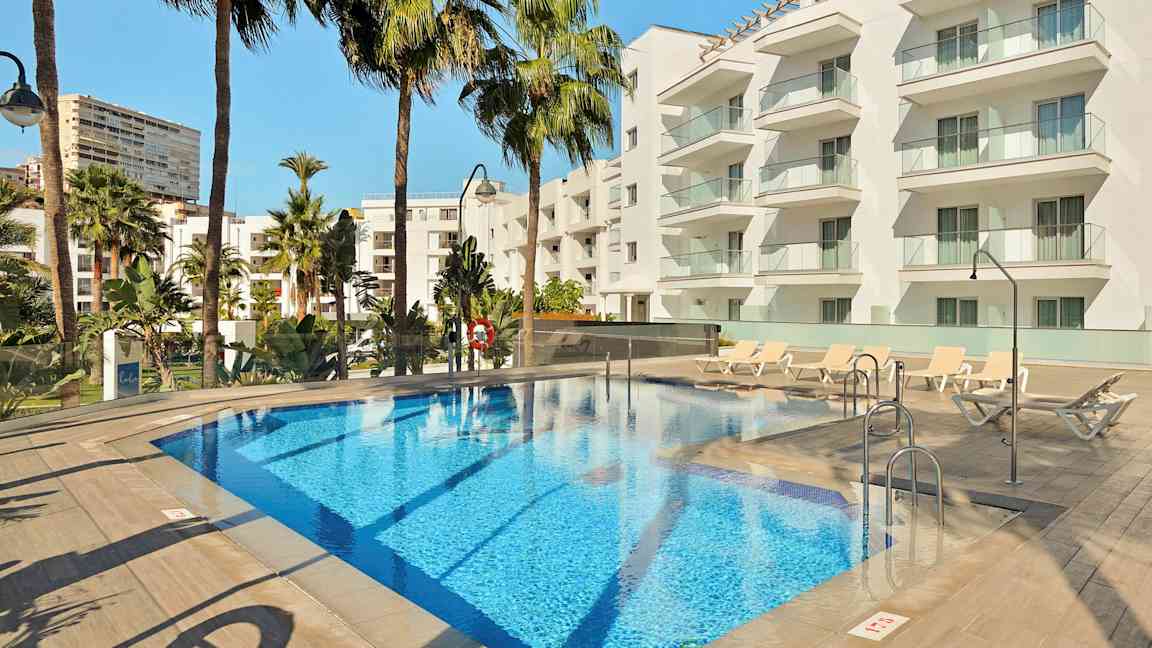 Hotellbasseng med solsenger og moderne hvite bygninger i bakgrunnen. (AI-generert tekst)