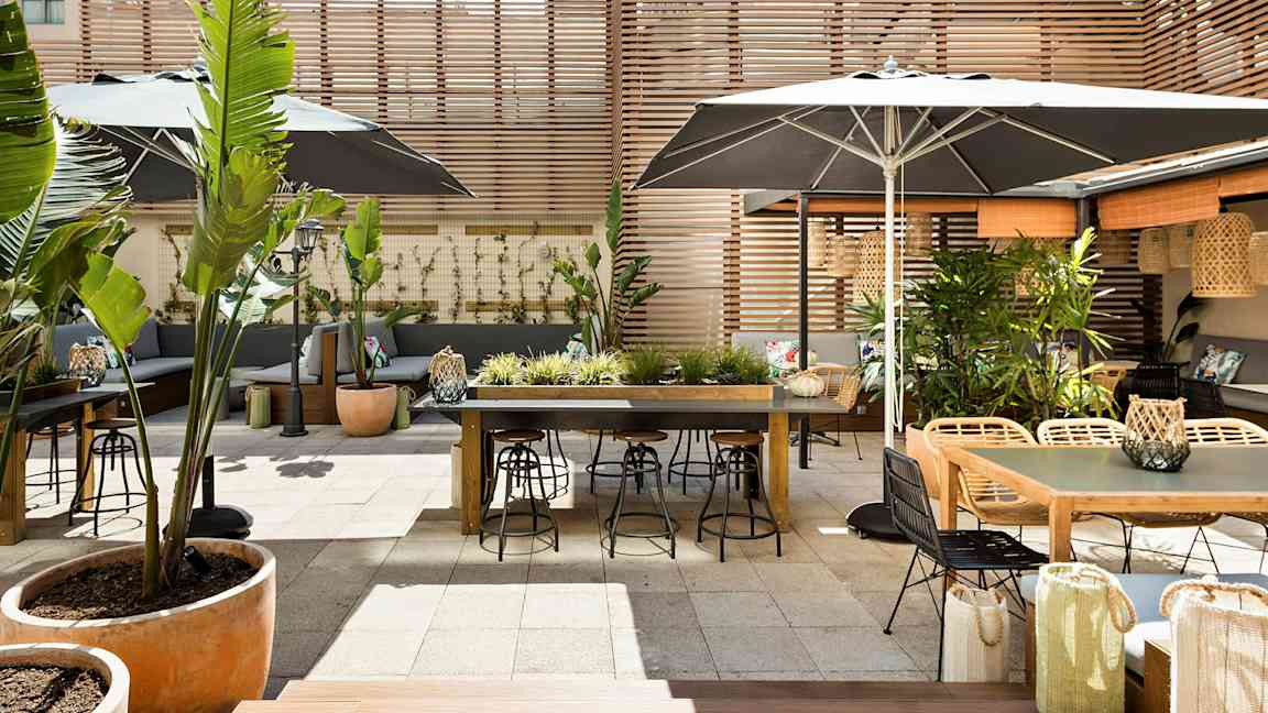 En utendørs terrasse med bord, stoler og plantepynt, omgitt av trepaneler. (AI-generert tekst)