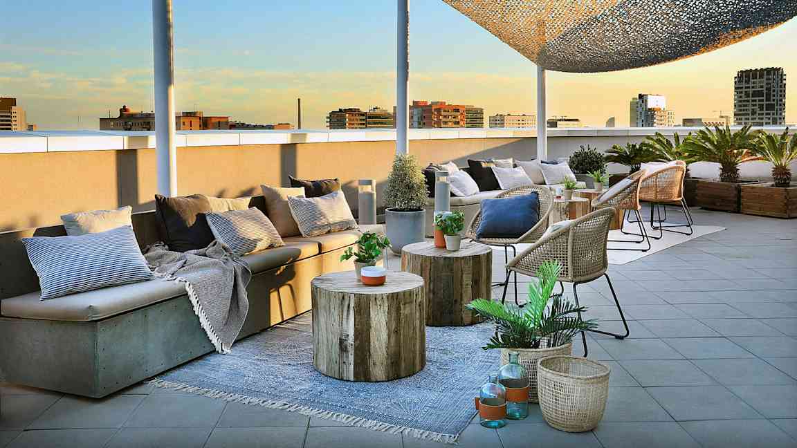 En takterrasse med sittemøbler, bord og kurver dekorert med planter og puter er avbildet. (AI-generert tekst)