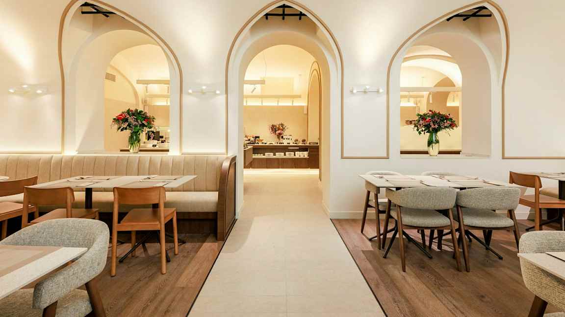 En elegant restaurant med bueformede vinduer, trestoler og bord samt blomsterdekorasjoner. (AI-generert tekst)
