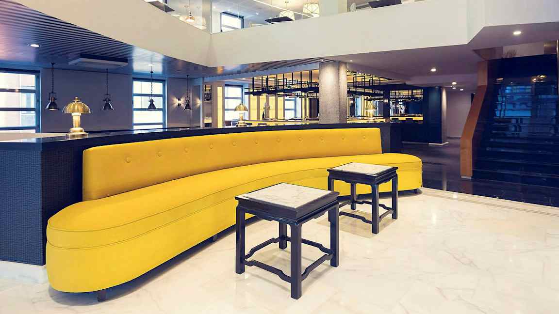 Et stilfullt innredet rom med en gul sofa, små bord og moderne belysning. (AI-generert tekst)