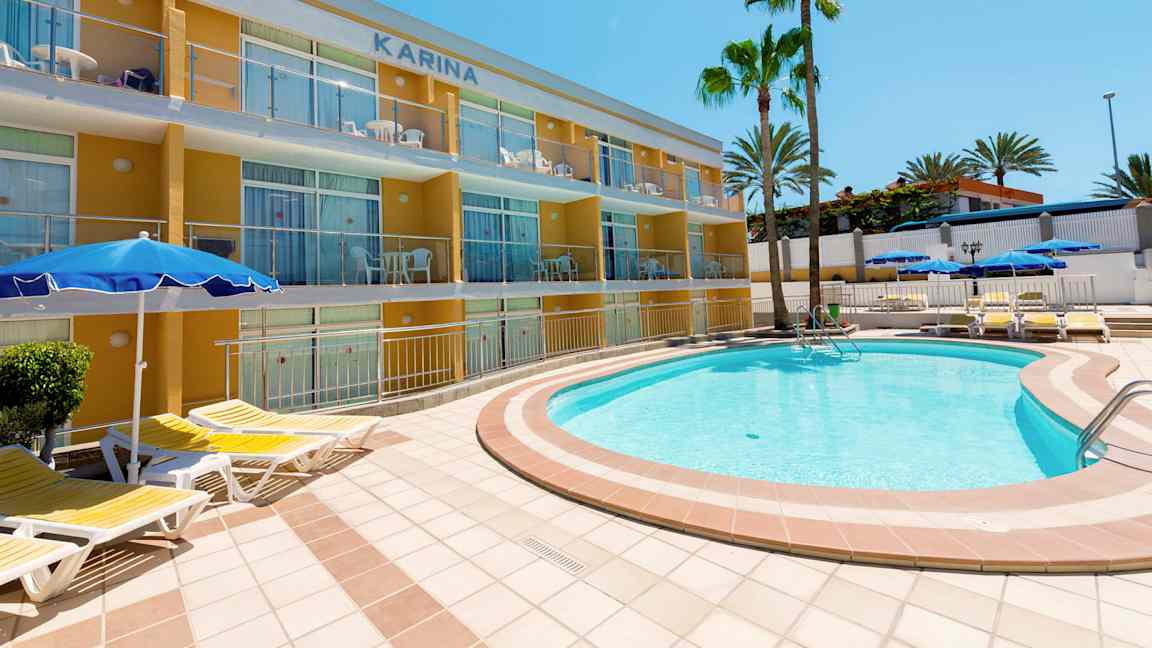 Et utendørs svømmebasseng med solsenger nær en leilighetsbygning og palmer. (AI-generert tekst)