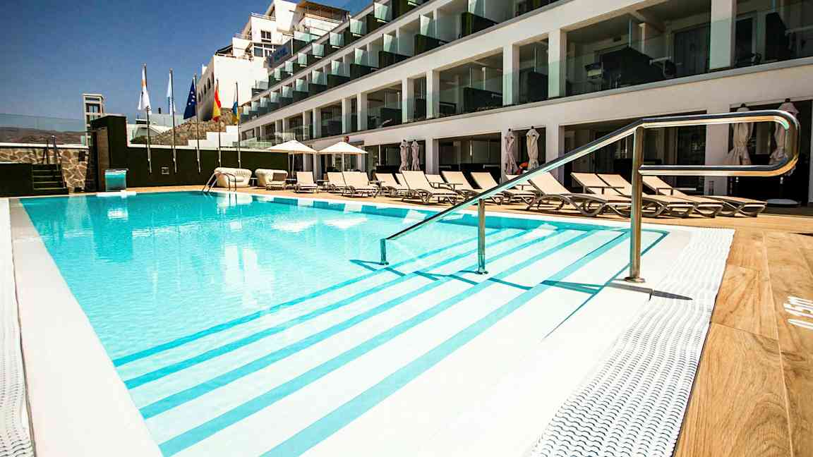 Utendørs basseng ved hotell med solsenger og glassbalkonger. (AI-generert tekst)