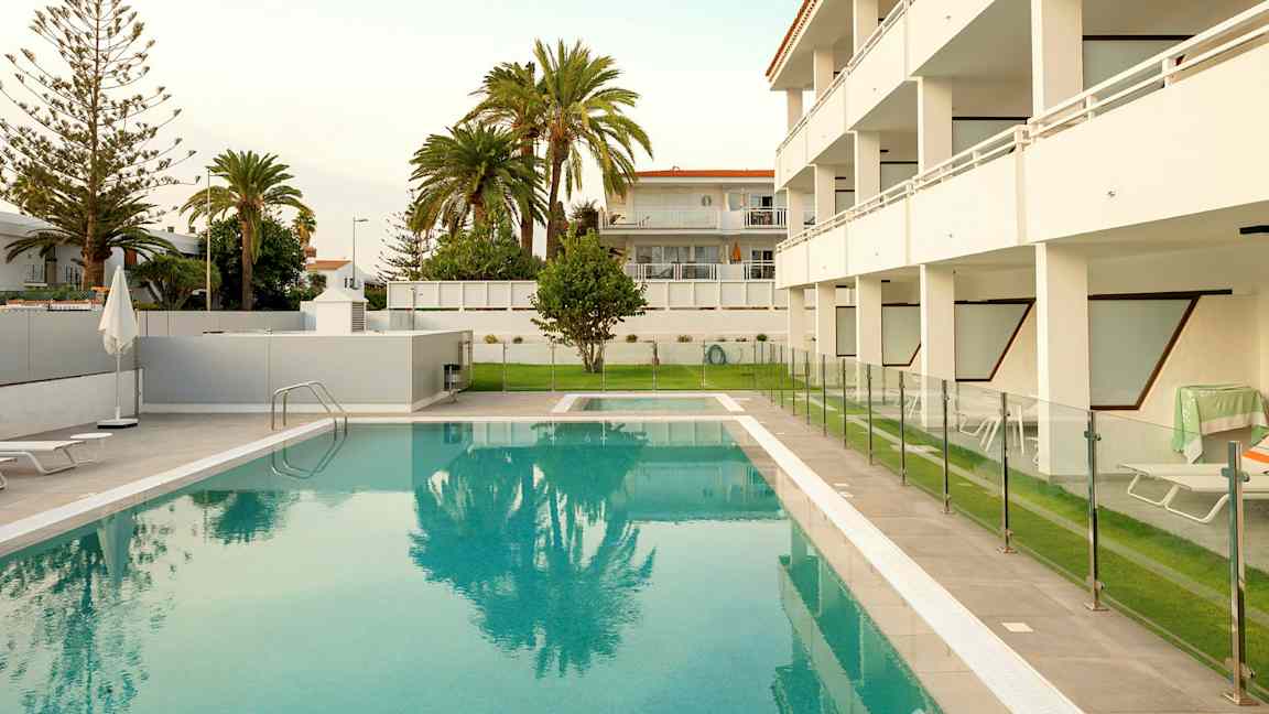 Utendørs svømmebasseng med gjerde og omkringliggende bygninger i bakgrunnen. (AI-generert tekst)