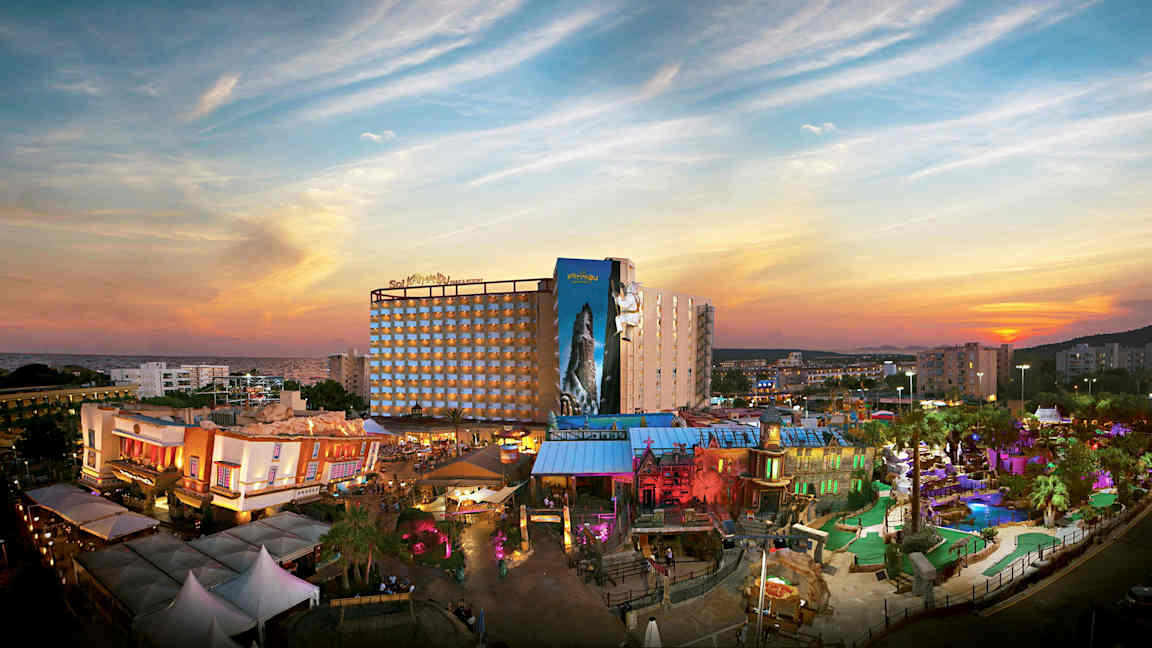 En utsikt over et feriehotell med en fargerik temapark foran en solnedgang. (AI-generert tekst)