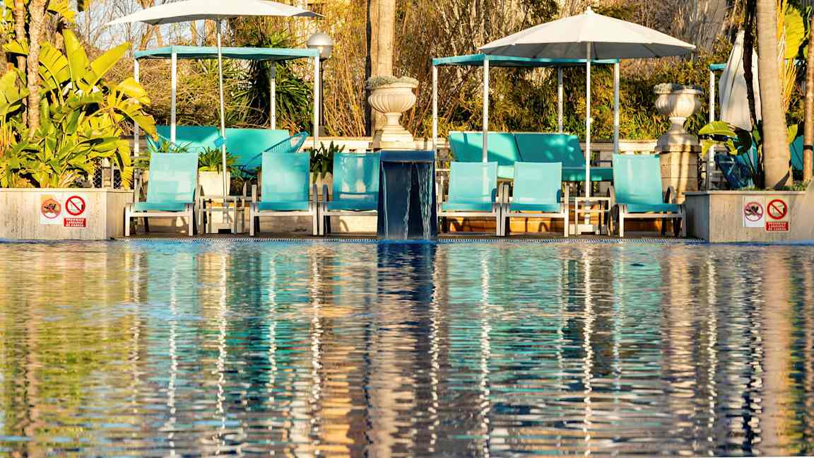 Solstoler ved et basseng med parasoller og grønne planter i bakgrunnen. (AI-generert tekst)