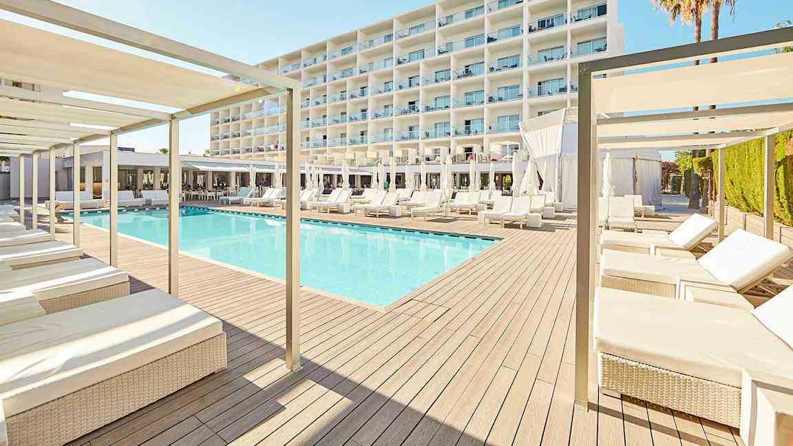 Et moderne hotellmiljø med et basseng omgitt av solsenger og parasoller, med en stor hvit bygning i bakgrunnen. (AI-generert tekst)