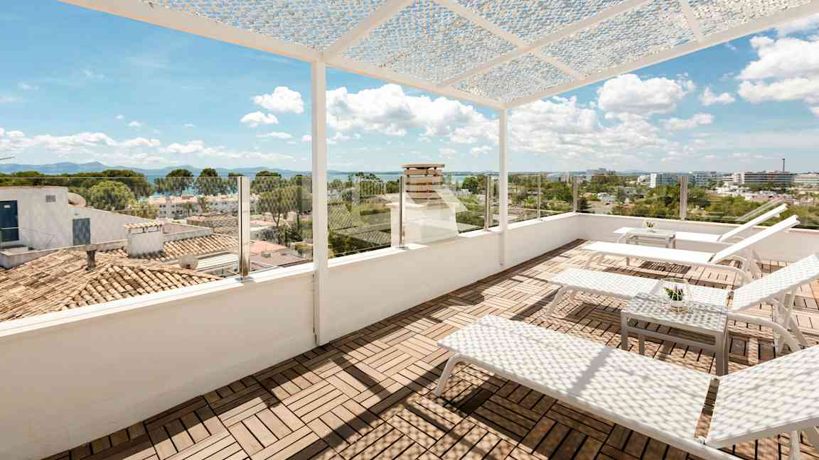En takterrasse med solsenger og et bord. Terrassen har en perforert takdekke og glassrekkverk med utsikt over byen og havet. (AI-generert tekst)