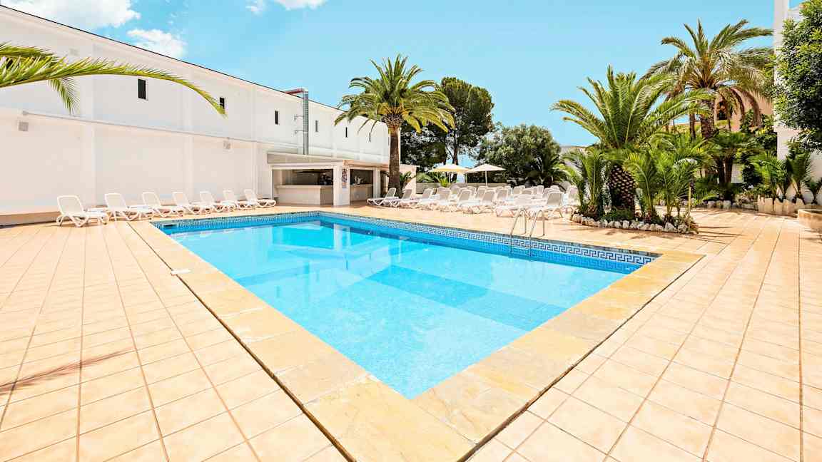 Bilde som viser et basseng med lyseblått vann, omgitt av en solterrasse med solsenger og palmer. (AI-generert tekst)