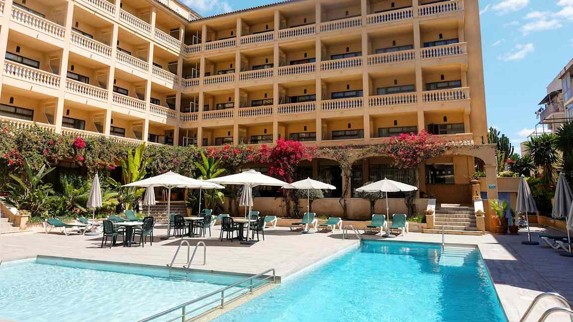 Hotell med flere etasjer og balkonger, bassengområde med solsenger og parasoller. (AI-generert tekst)