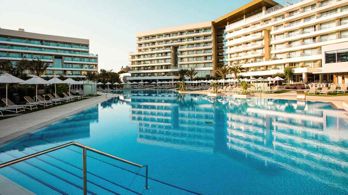 Utendørs basseng ved et hotell med solsenger og parasoller, omgitt av bygninger med flere etasjer. (AI-generert tekst)