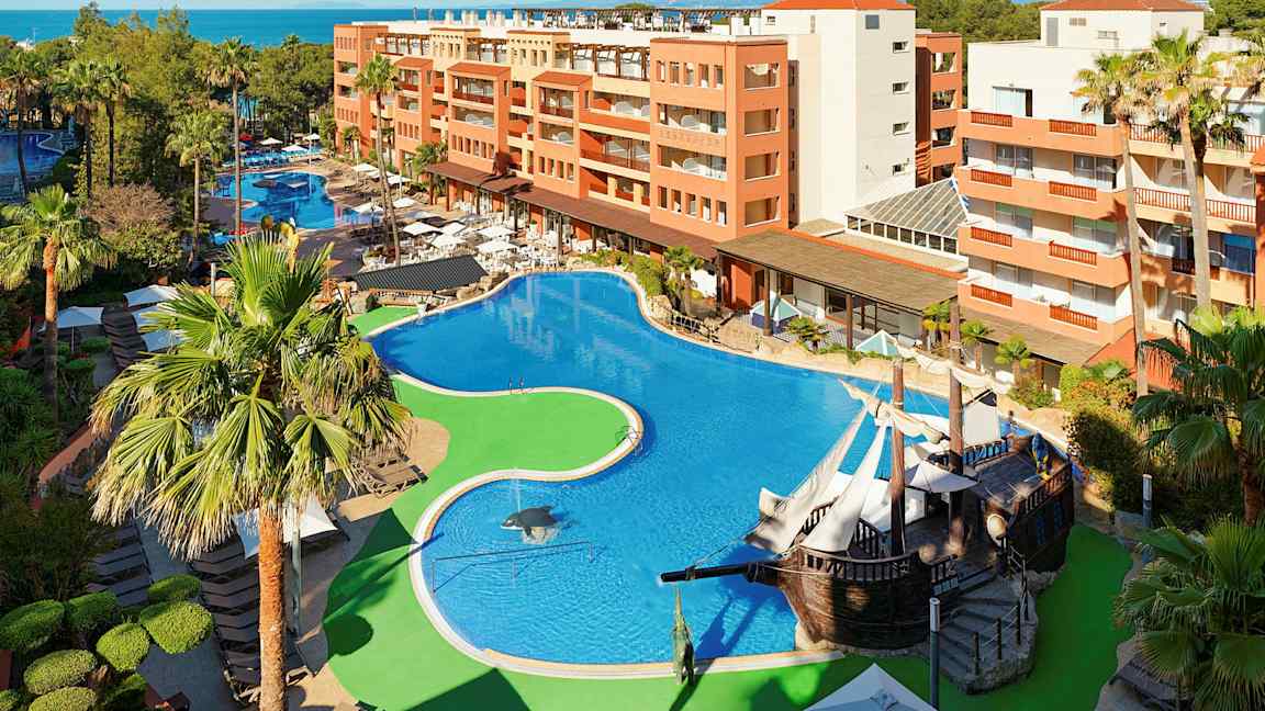 Hotellområde med stort basseng, omgitt av palmer og bygninger. (AI-generert tekst)