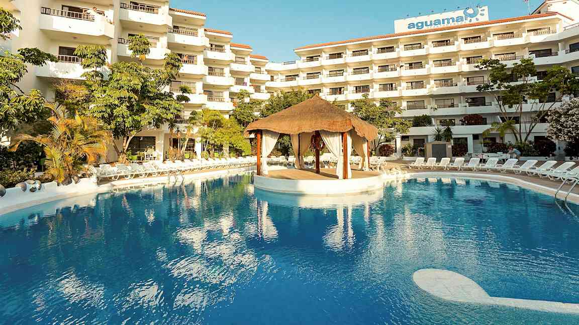 Hotellkompleks med flere etasjer, et stort basseng og en takhyttestruktur i midten av bassenget. (AI-generert tekst)