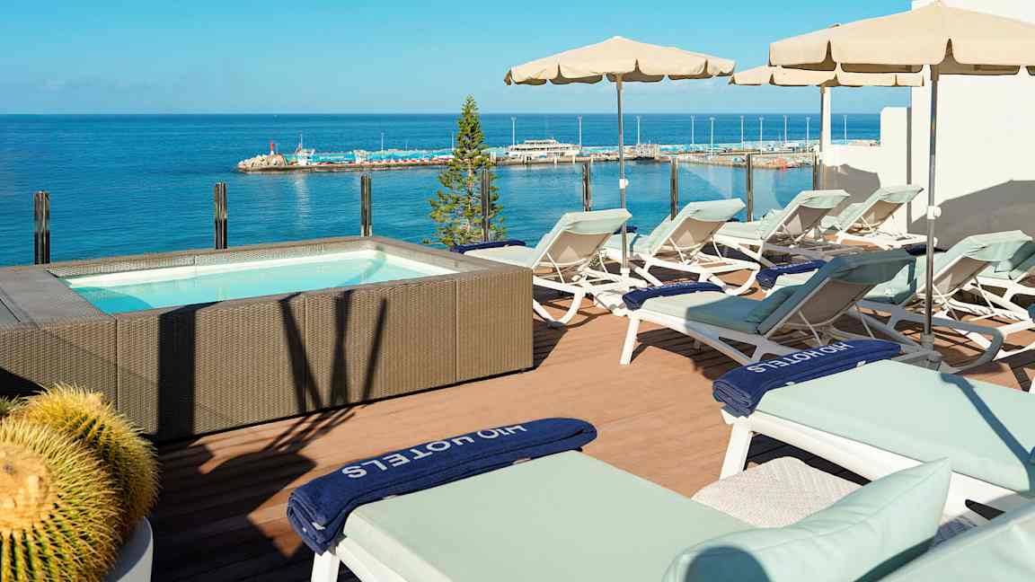Terrasse med solsenger og parasoller ved et boblebad med havutsikt. (AI-generert tekst)