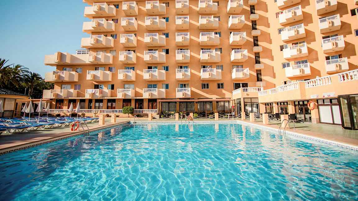 Bygning med flere balkonger og et stort basseng foran. (AI-generert tekst)