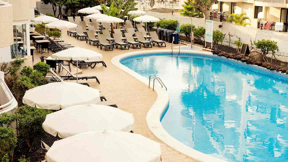 Bassengområde med solsenger og parasoller ved et hotell. (AI-generert tekst)