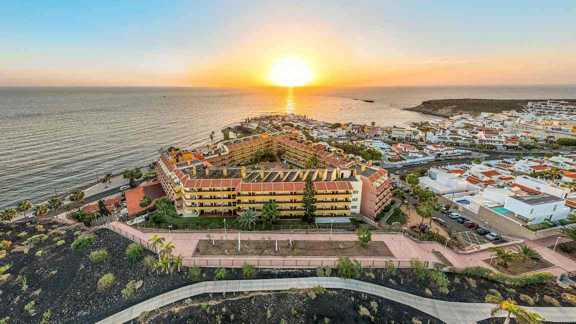 Utsikt ovenfra av en solnedgang over havet og et ferieanlegg med bygninger og gangveier. (AI-generert tekst)