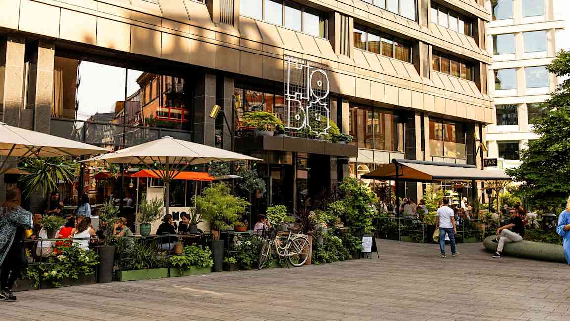 En uteservering foran en moderne bygning med store glassvinduer. (AI-generert tekst)