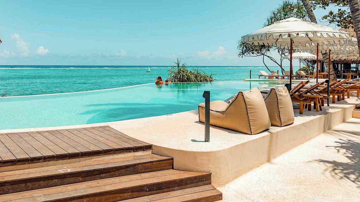 Et evighetsbasseng ved havet, omgitt av solsenger og parasoller. (AI-generert tekst)