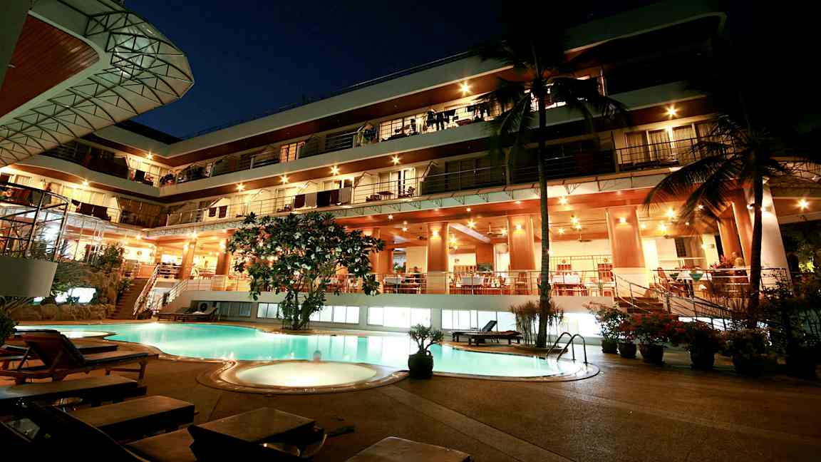 Kveldsvy av en fleretasjes bygning med opplyst fasade og et basseng i forgrunnen. (AI-generert tekst)