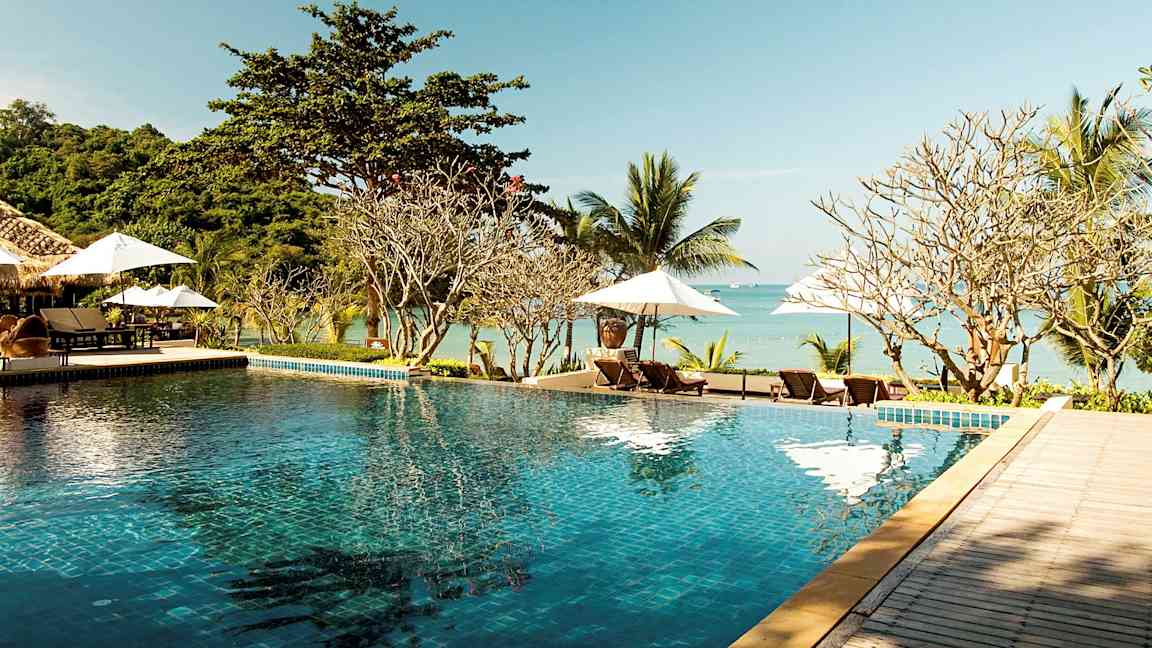 Et infinitybasseng ved en strand med solsenger og parasoller i bakgrunnen. (AI-generert tekst)