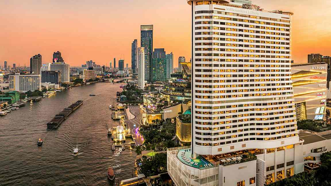 Utsikt over en elv omgitt av høye bygninger under en solnedgang. Et stort hotell er synlig i forgrunnen. (AI-generert tekst)