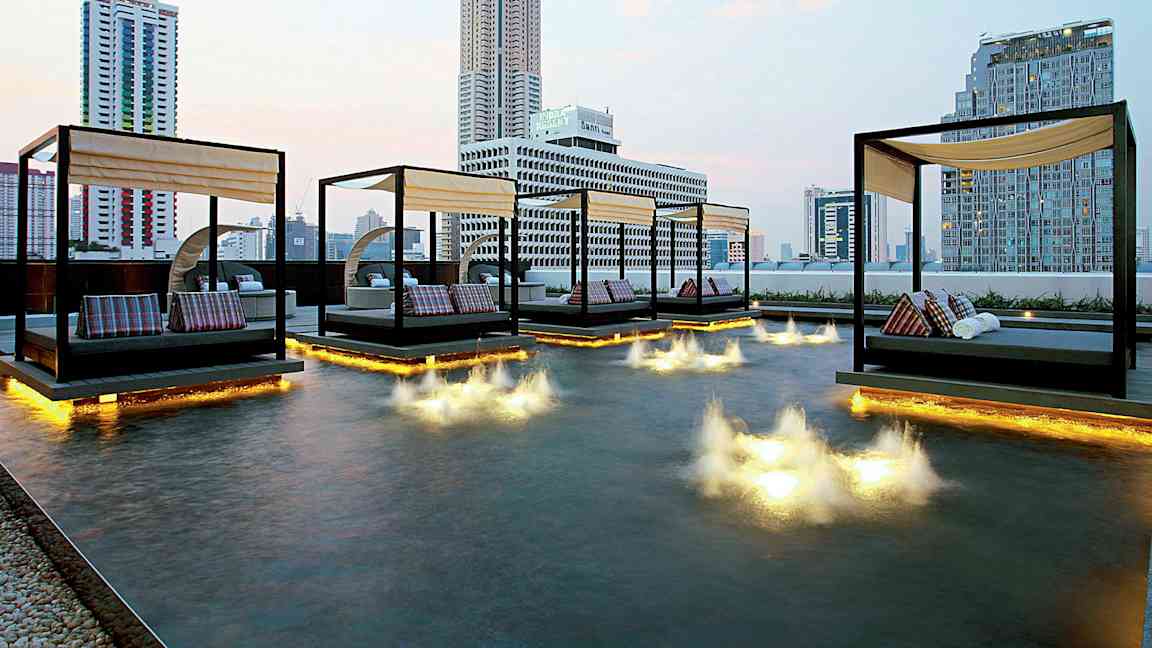 Bilde av en moderne byutsikt med dagsenger plassert over et grunt basseng med lysinstallasjoner i vannet. (AI-generert tekst)