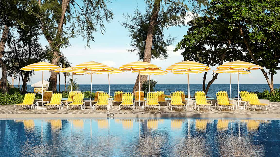 Et basseng foran solsenger med gule og hvite parasoller ved sjøen. (AI-generert tekst)