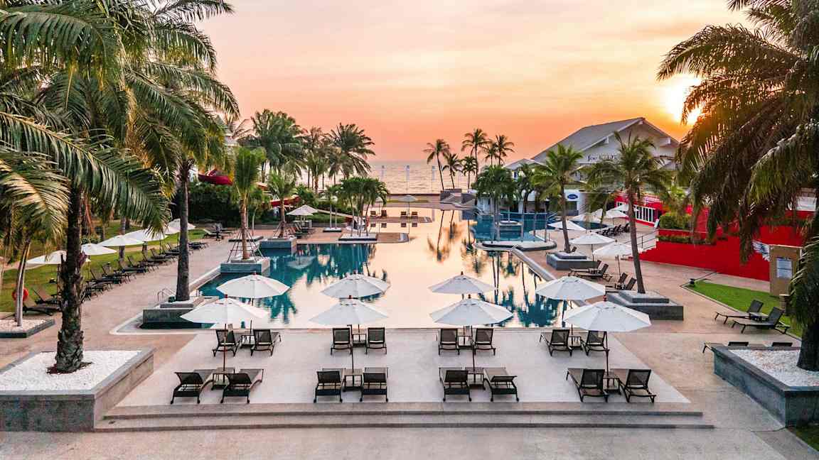 Et basseng med solsenger og parasoller ved solnedgang. (AI-generert tekst)