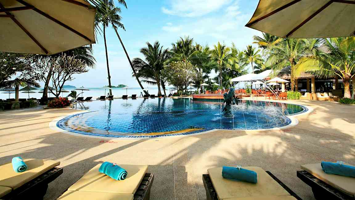 Et basseng omgitt av palmer og solsenger med utsikt over havet og en blå himmel. (AI-generert tekst)