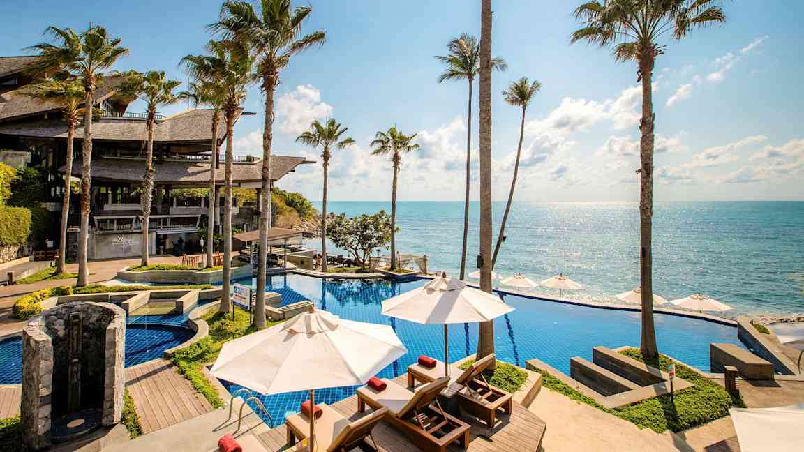 Et bassengområde ved havet med fantastisk utsikt over blått vann, omgitt av høye palmer. (AI-generert tekst)