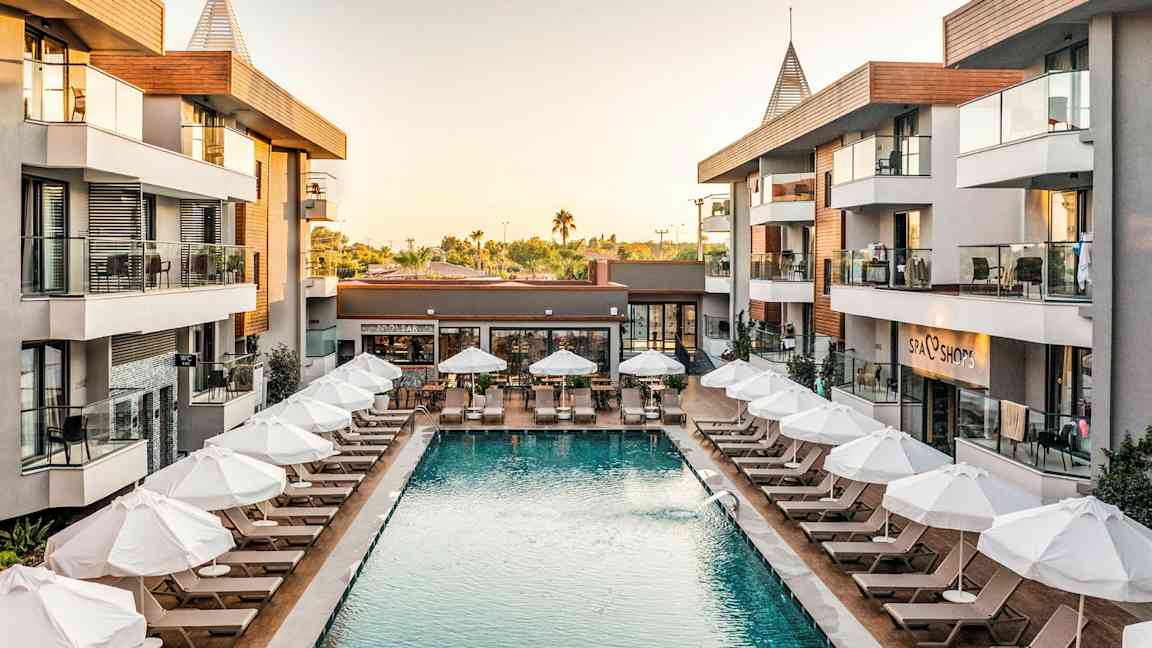 Hotellområde med basseng og solsenger omgitt av bygninger. (AI-generert tekst)