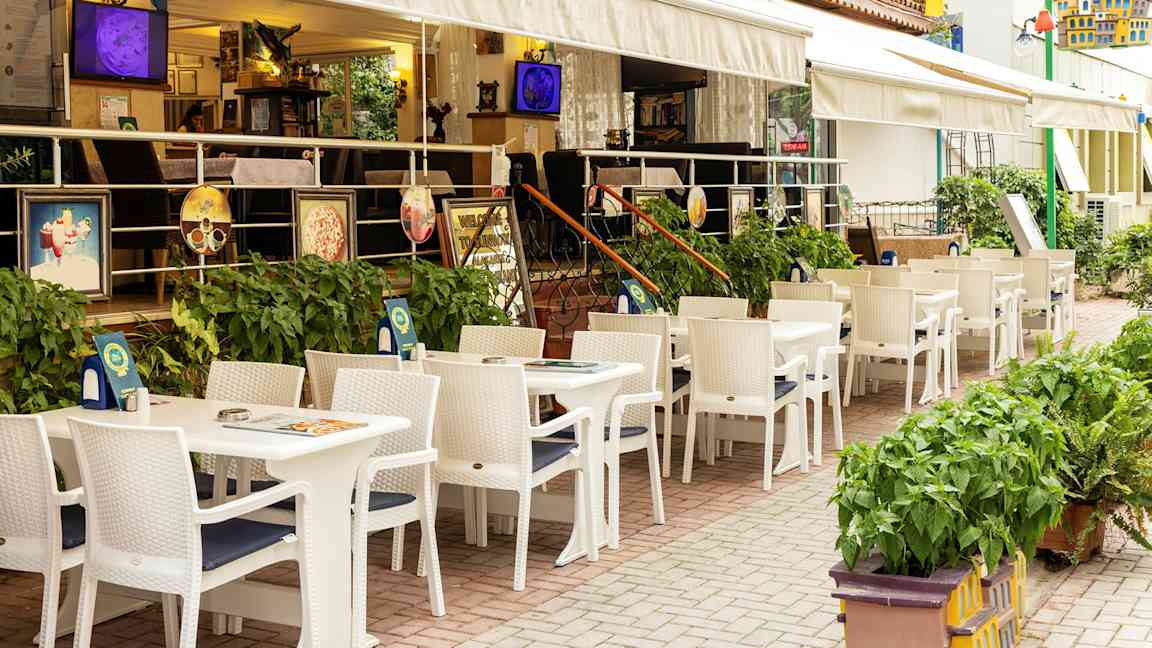 Restaurant med uteservering med hvite bord og stoler ved et hotell. (AI-generert tekst)