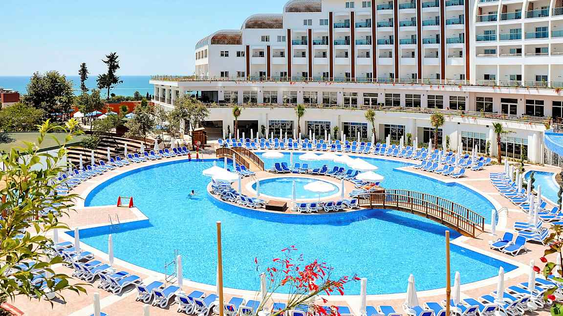 Hotell med stort basseng og solsenger ved havet. (AI-generert tekst)