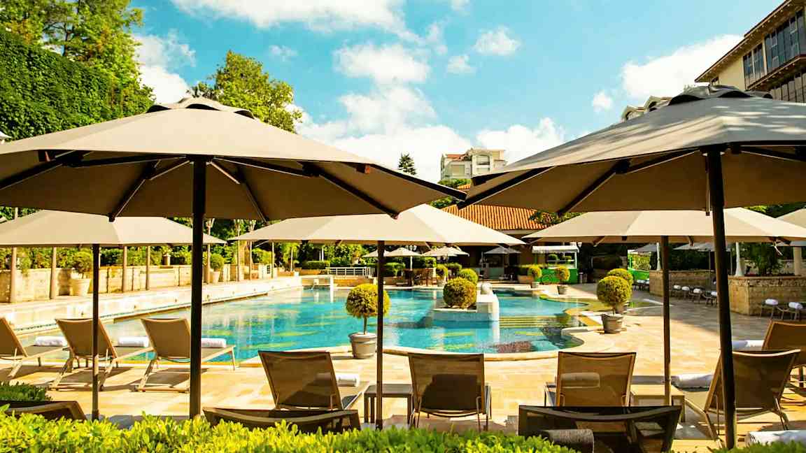 Bassengområde med parasoller, solsenger og omkringliggende grøntområder. (AI-generert tekst)