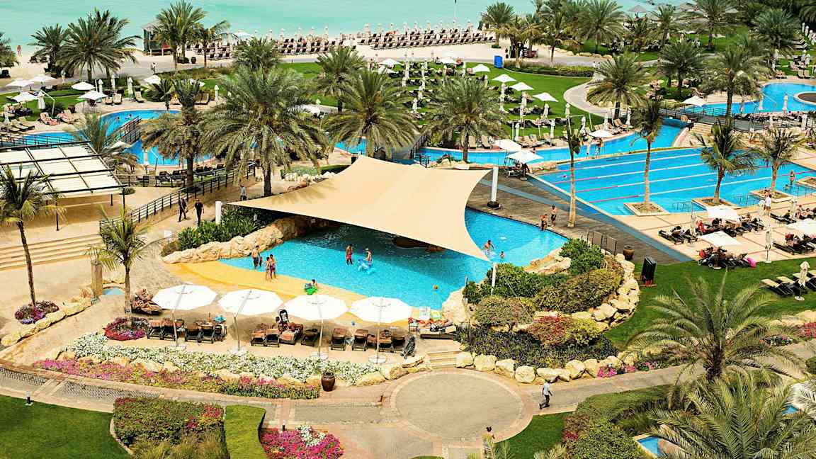 Et feriested med bassengområde nær stranden, omgitt av palmer og solsenger. (AI-generert tekst)