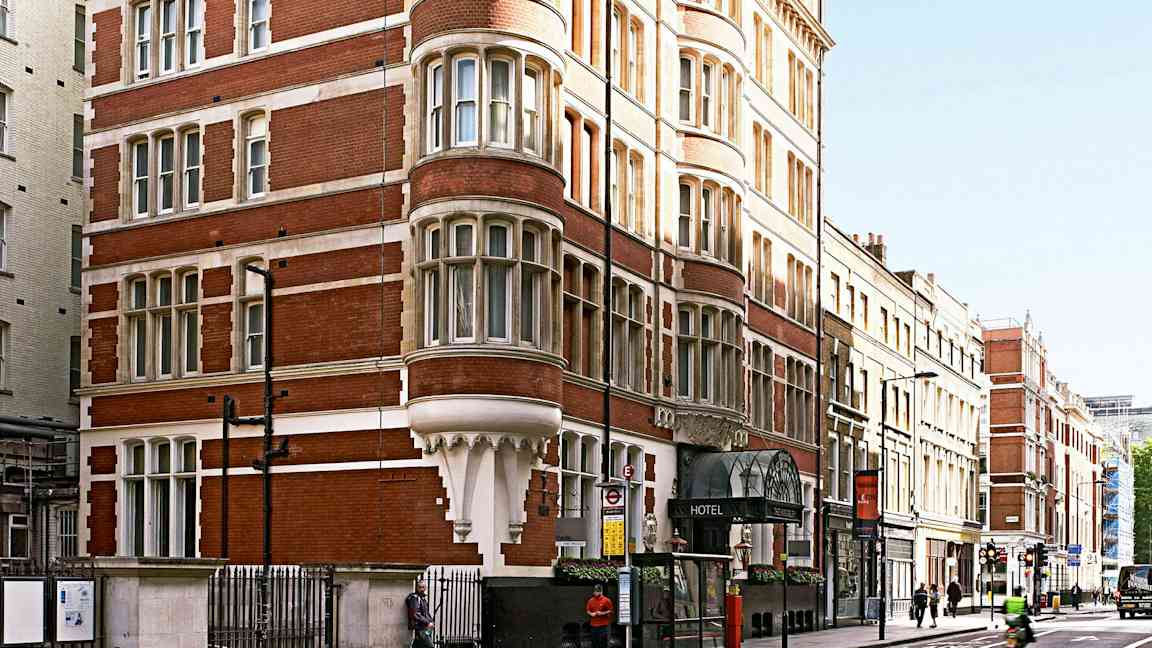 Et bilde av en rød murbygning med mange vinduer og et hotell i første etasje. (AI-generert tekst)