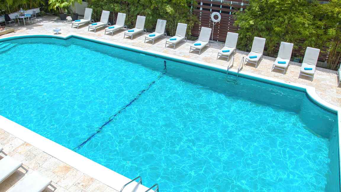 Et basseng omgitt av solsenger og grøntområder. (AI-generert tekst)