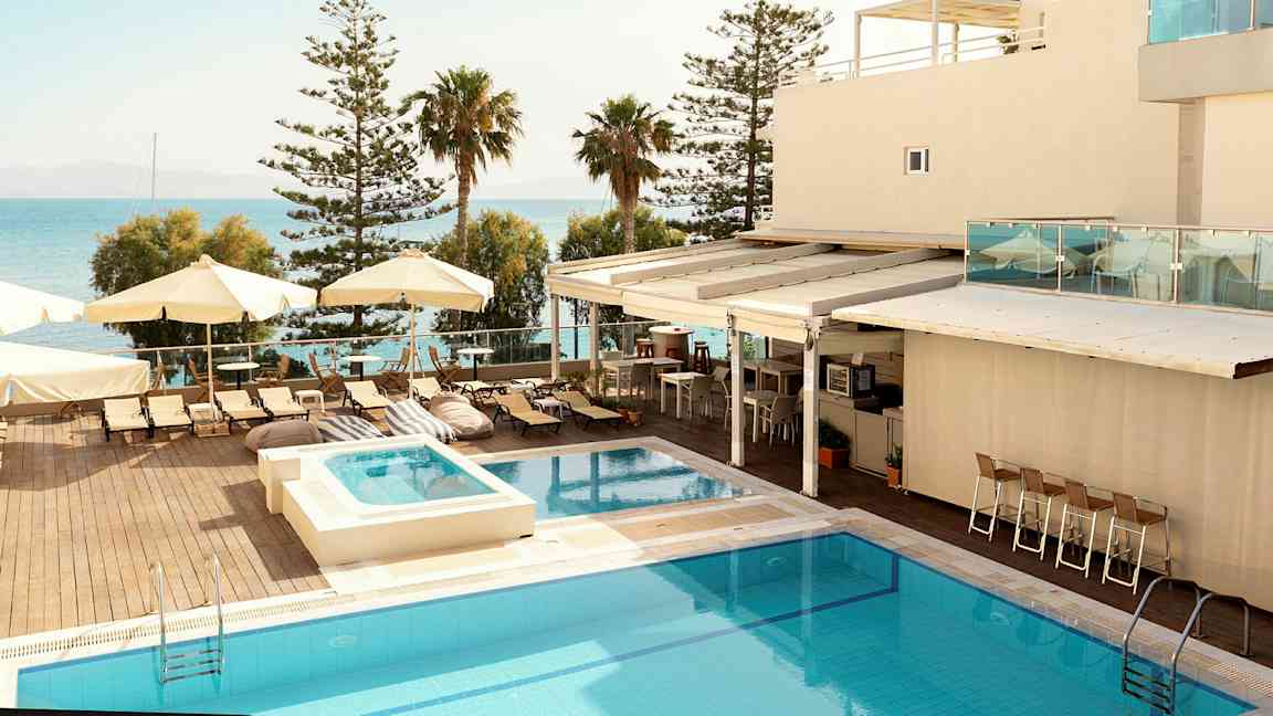 Et hotellområde med et basseng, solsenger og parasoller ved havet. (AI-generert tekst)