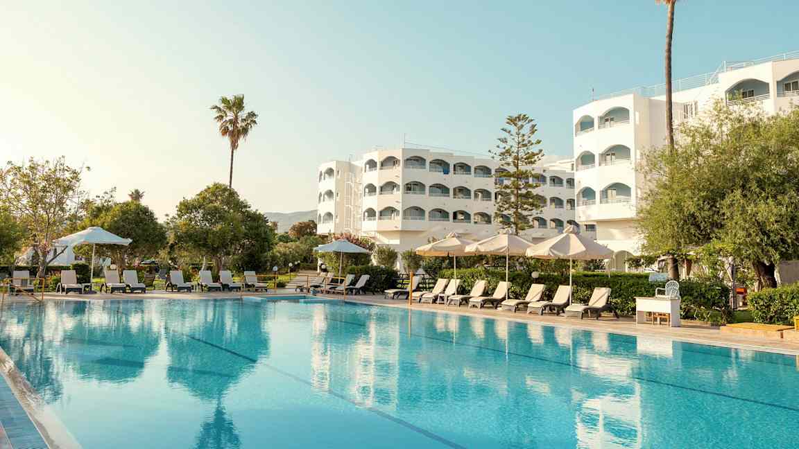 Hotellbygning med basseng, solsenger og parasoller i forgrunnen. (AI-generert tekst)
